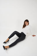 Pantalon slim enduit noir à coupe ajustée porté avec un haut blanc.