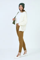 Pantalon slim push-up couleur camel porté avec un cardigan blanc et un bonnet vert.