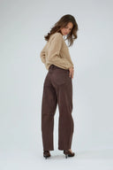 Jean barrel marron à coupe large et taille haute porté avec un pull beige.